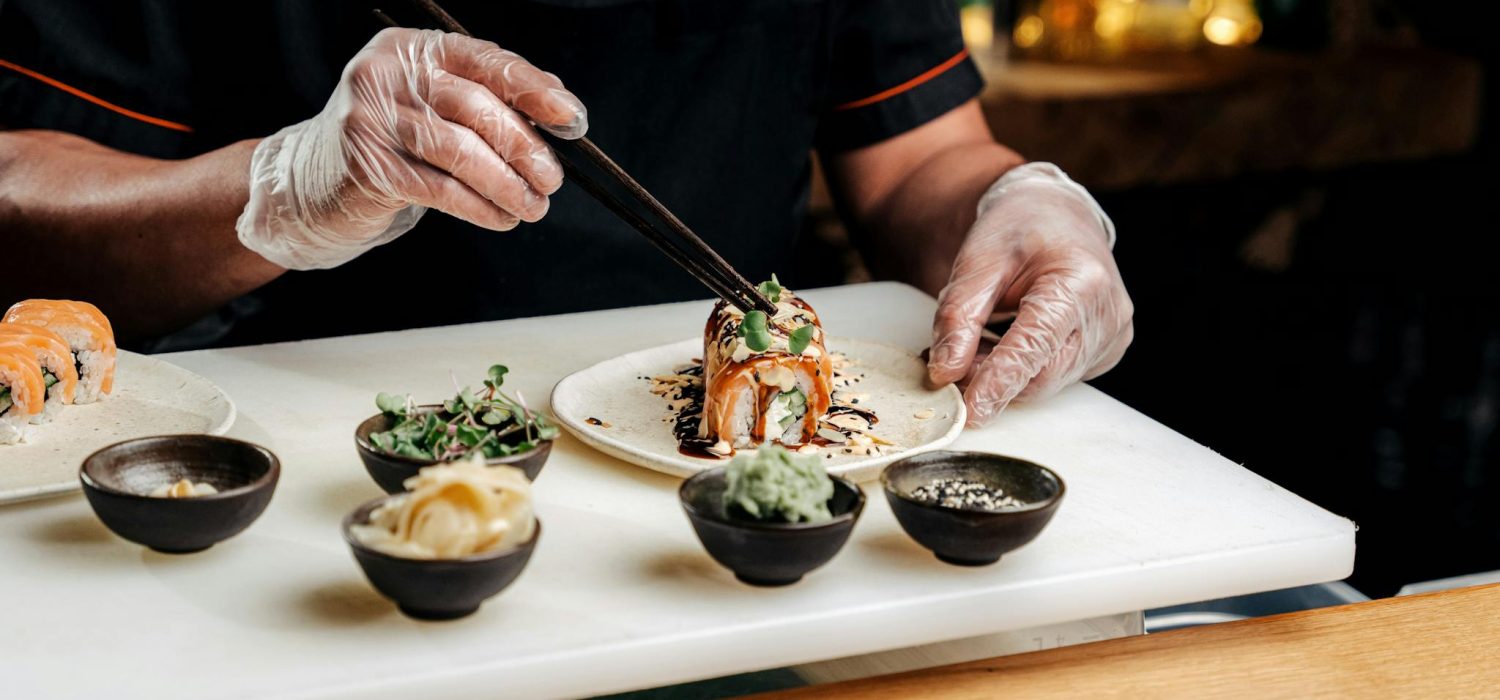 A professional chef artfully organizes sushi with chopsticks, showcasing traditional Japanese cuisine preparation.
